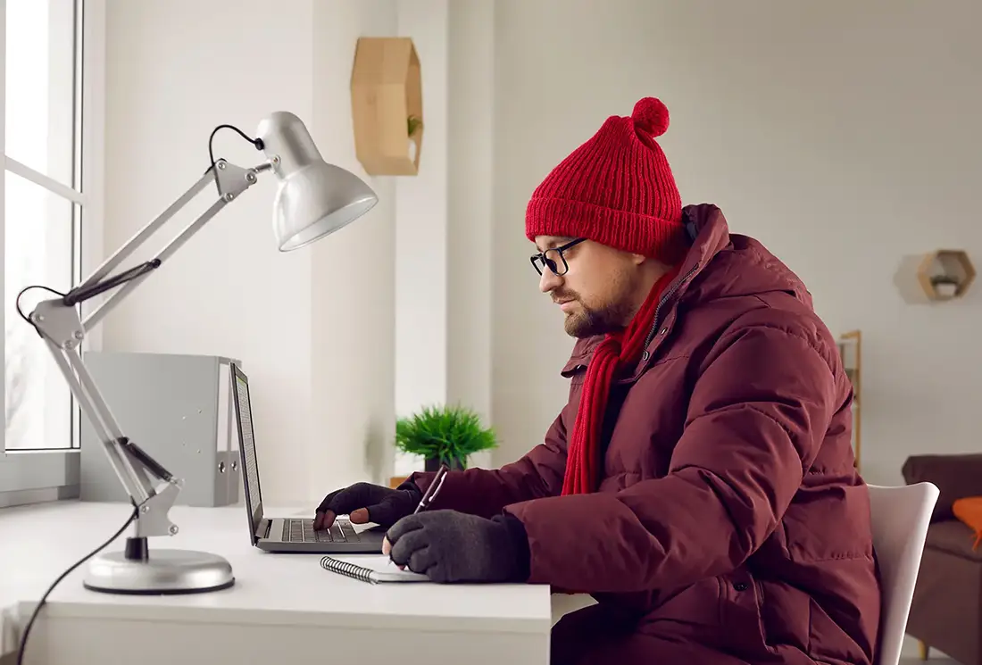 Frysande man i varm vinterjacka och handskar som arbetar på bärbar dator